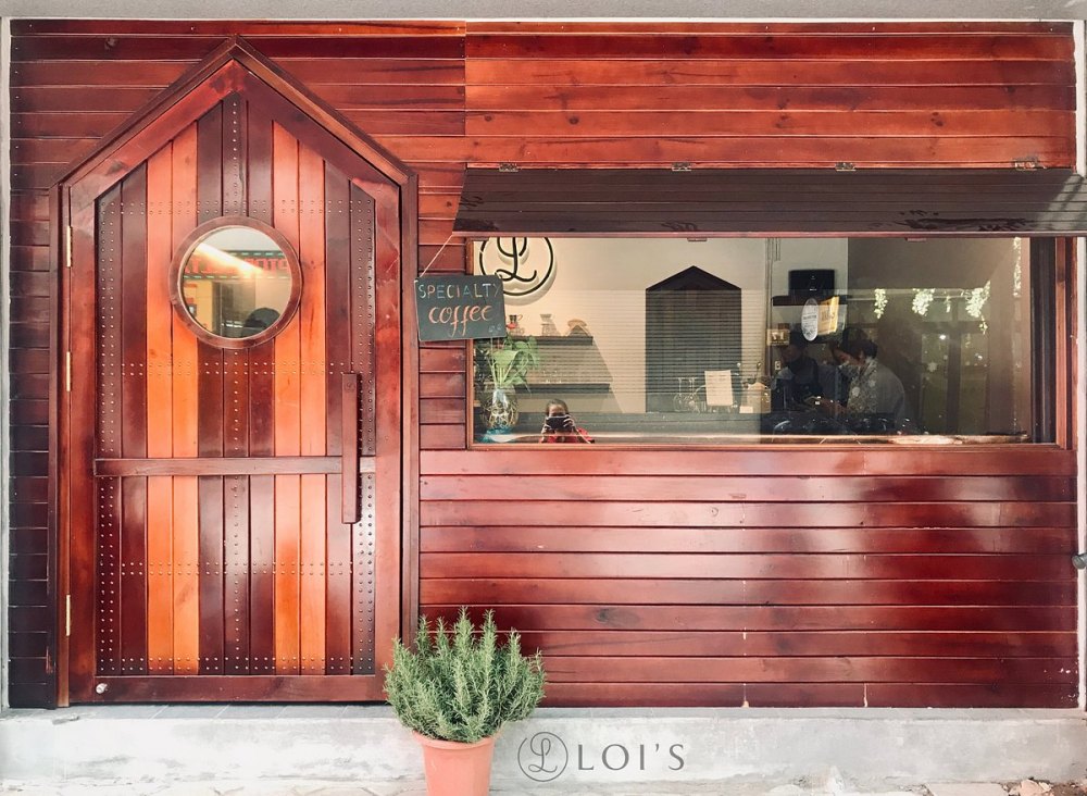 Cửa gỗ và cửa sổ quán cà phê, có biển "Specialty coffee" và chậu cây trang trí phía trước.