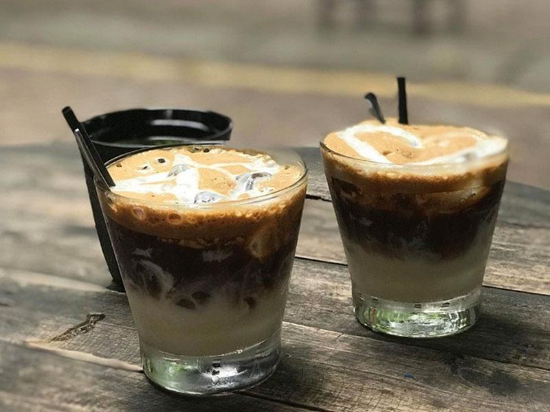cach-lam-bac-xiu-4-tang-7 Hai ly cà phê sữa đá với ống hút đen trên bàn gỗ, lớp bọt kem bên trên.