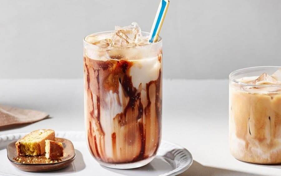 Ly c&agrave; ph&ecirc; sữa đ&aacute; với lớp sốt chocolate, ống h&uacute;t m&agrave;u sắc, b&ecirc;n cạnh l&agrave; b&aacute;nh quy v&agrave; ly c&agrave; ph&ecirc; kh&aacute;c.