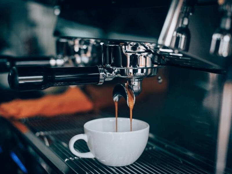 Máy pha cà phê đang chảy nước cà phê vào một chiếc tách trắng.
