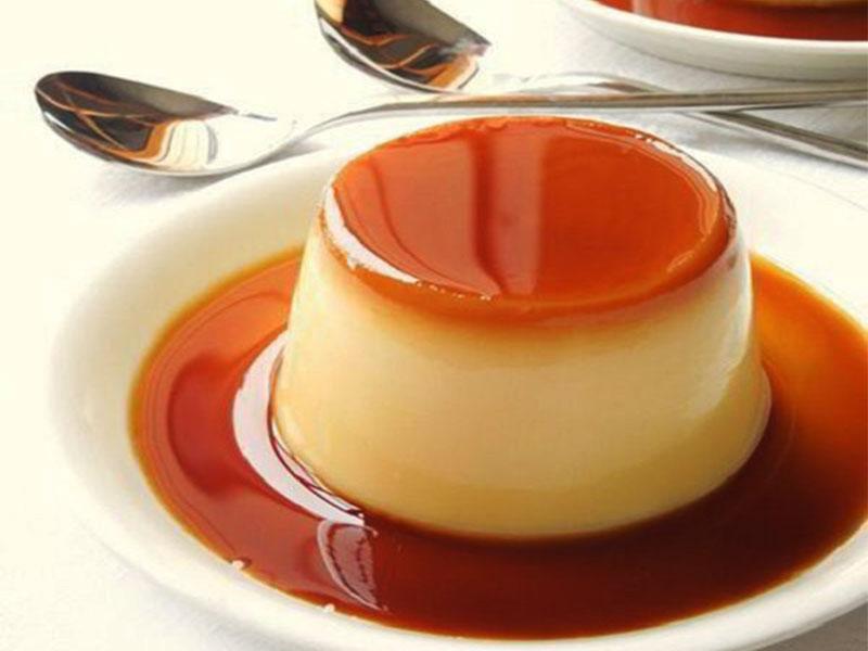 cach-lam-sot-ca-phe-an-banh-flan-3 Bánh flan caramel trên đĩa trắng, có lớp caramel màu nâu bóng láng, cạnh đó là hai muỗng kim loại.