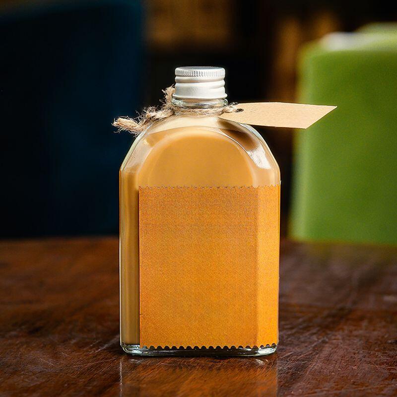 cach-pha-ca-phe-dong-chai-2 Chai thủy tinh chứa chất lỏng màu nâu nhạt, có nắp kim loại và thẻ nhãn giấy buộc dây, đặt trên bề mặt gỗ.