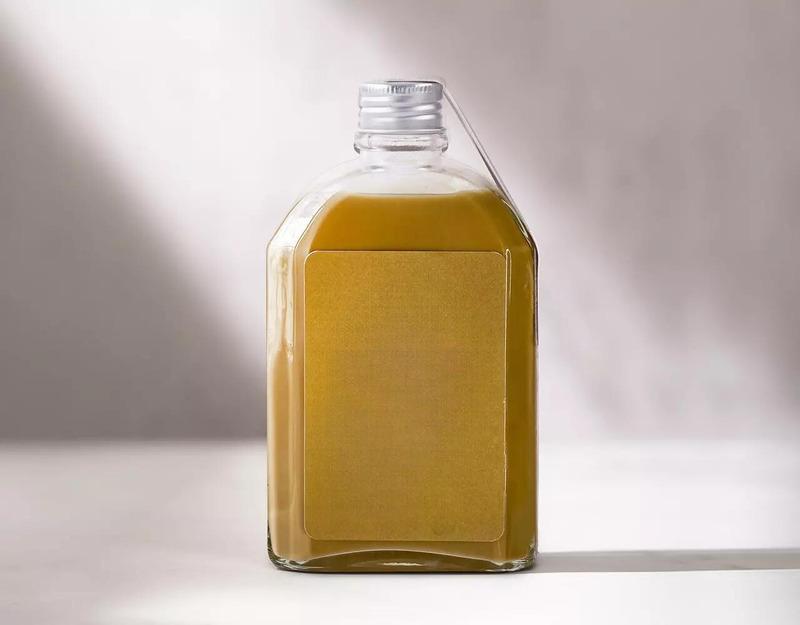 cach-pha-ca-phe-dong-chai-3 Chai thủy tinh chứa chất lỏng màu vàng nhạt, nắp vặn bạc, đặt trên nền màu trắng xám.