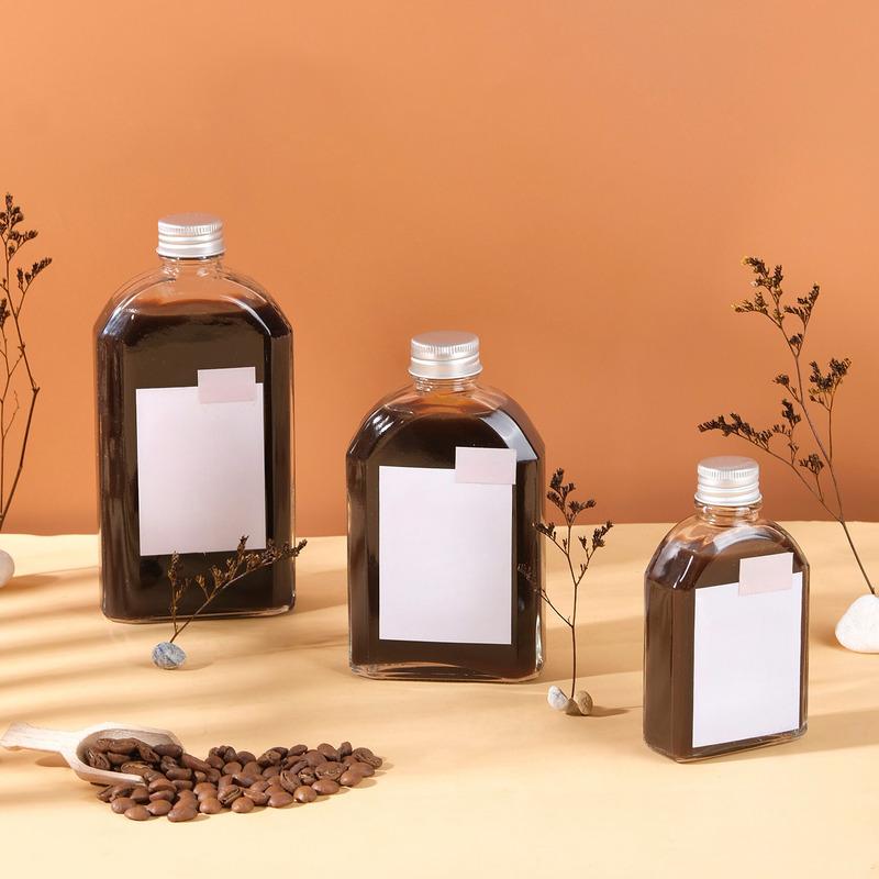 cach-pha-ca-phe-dong-chai-4 Ba chai thủy tinh chứa chất lỏng màu nâu, với nhãn trắng, xung quanh có hạt cà phê và cành khô trang trí.