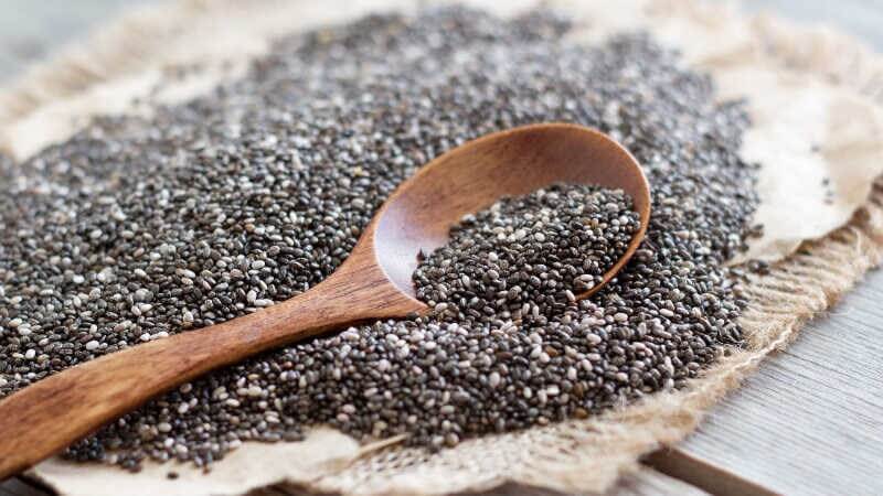 Hạt chia đen nằm trên nền vải, với một chiếc muỗng gỗ đặt trên bề mặt.