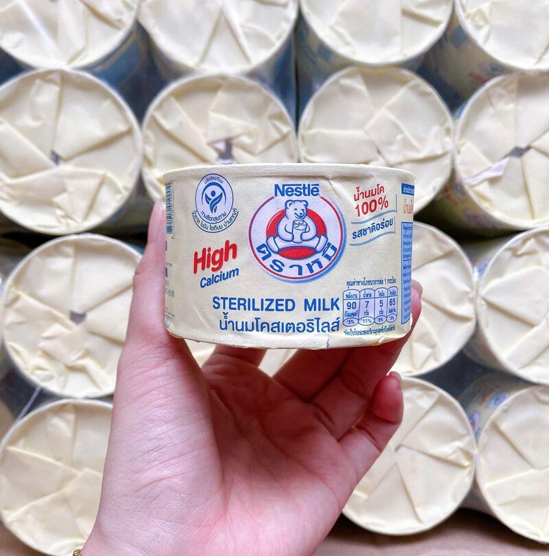 Hộp sữa tiệt tr&ugrave;ng Nestle được cầm tr&ecirc;n tay, nền l&agrave; nhiều hộp sữa kh&aacute;c xếp chồng l&ecirc;n nhau.