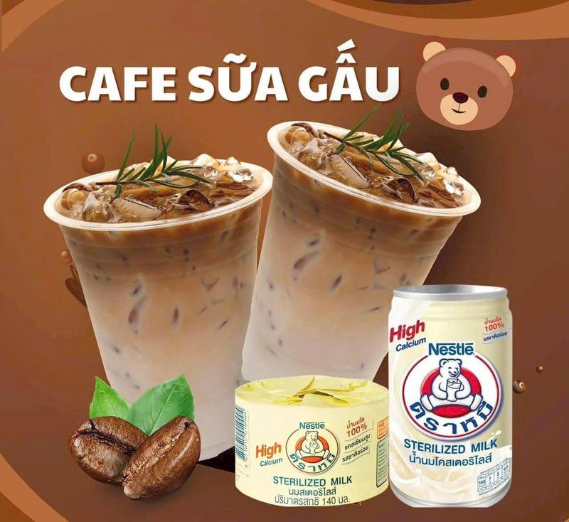 Hai ly c&agrave; ph&ecirc; sữa đ&aacute; với hộp v&agrave; lon sữa tiệt tr&ugrave;ng, nền n&acirc;u, c&oacute; h&igrave;nh minh họa hạt c&agrave; ph&ecirc; v&agrave; l&aacute;.