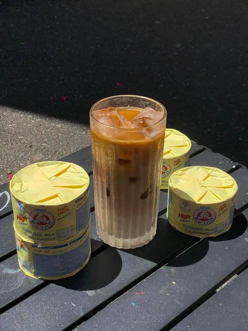 Ly c&agrave; ph&ecirc; sữa đ&aacute; đặt tr&ecirc;n b&agrave;n, b&ecirc;n cạnh l&agrave; ba hộp sữa đặc m&agrave;u v&agrave;ng.