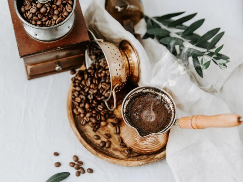 Cà phê phin truyền thống với hạt cà phê, máy xay và lá trang trí trên nền vải trắng.