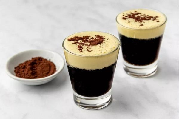 Hai ly cà phê trứng với lớp bọt kem trên mặt, bên cạnh là đĩa nhỏ chứa bột cacao.