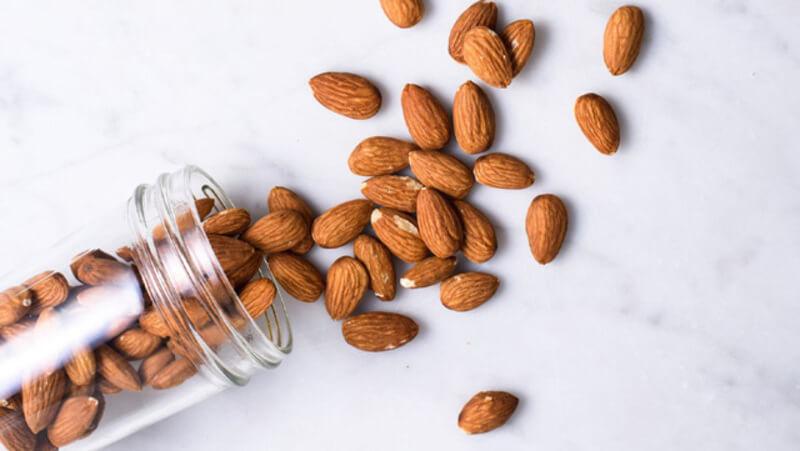 Hạt hạnh nhân đổ ra từ lọ thủy tinh trên nền trắng.