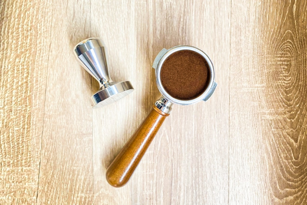 Tay cầm pha c&agrave; ph&ecirc; v&agrave; dụng cụ n&eacute;n, đặt tr&ecirc;n bề mặt gỗ s&aacute;ng m&agrave;u.