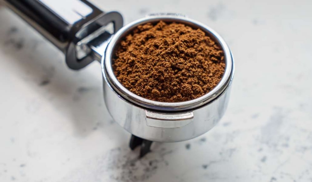 Tay cầm m&aacute;y pha c&agrave; ph&ecirc; chứa đầy bột c&agrave; ph&ecirc; tr&ecirc;n nền đ&aacute; m&agrave;u s&aacute;ng.