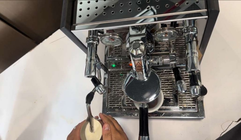 M&aacute;y pha c&agrave; ph&ecirc; espresso đang hoạt động, c&oacute; người đang tạo bọt sữa bằng v&ograve;i hơi.