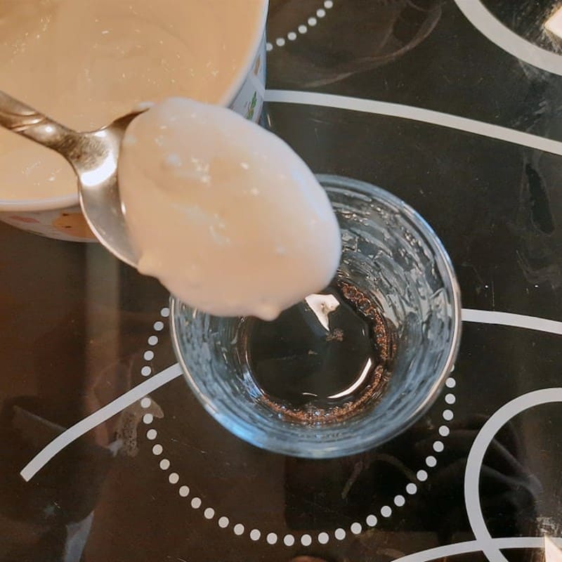 Cái muỗng đang múc sữa chua từ tô vào ly thủy tinh trong suốt trên bàn có hoa văn.