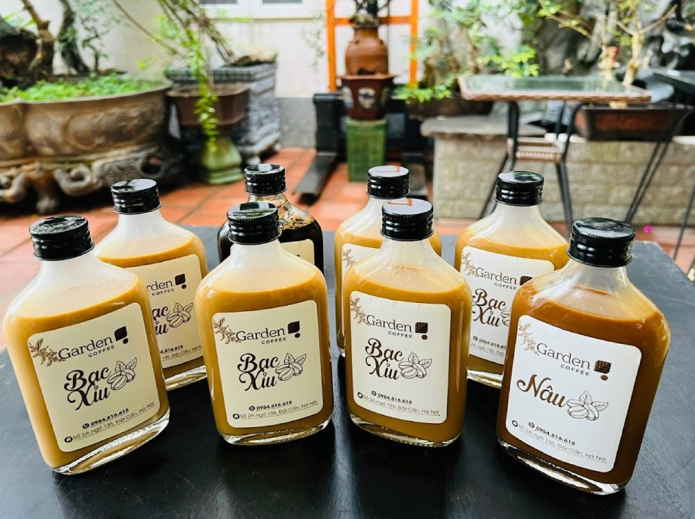 Khám Phá 11 Quán Cafe Đội Cấn Tuyệt Vời Cho Thư Giãn Và Làm Việc 11 Các chai cà phê nhãn "Garden Coffee", chứa đồ uống màu nâu, xếp trên bàn ngoài trời.