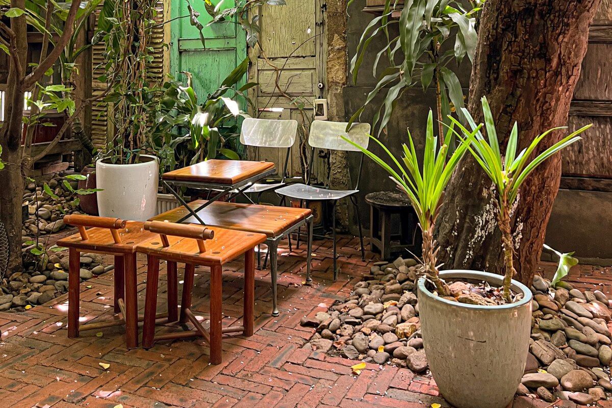 Khu vực ngoài trời với bàn ghế gỗ, cây xanh và sỏi, tạo không gian thư giãn tự nhiên.