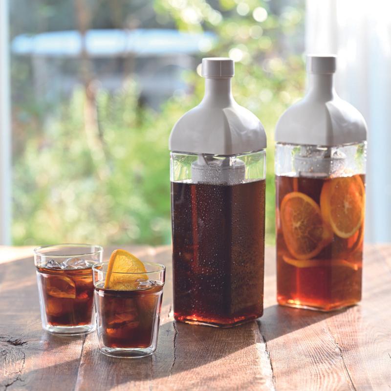 Hai ly tr&agrave; đ&aacute; cam l&aacute;t v&agrave; hai b&igrave;nh tr&agrave; lớn tr&ecirc;n b&agrave;n gỗ, &aacute;nh s&aacute;ng tự nhi&ecirc;n từ cửa sổ chiếu v&agrave;o.