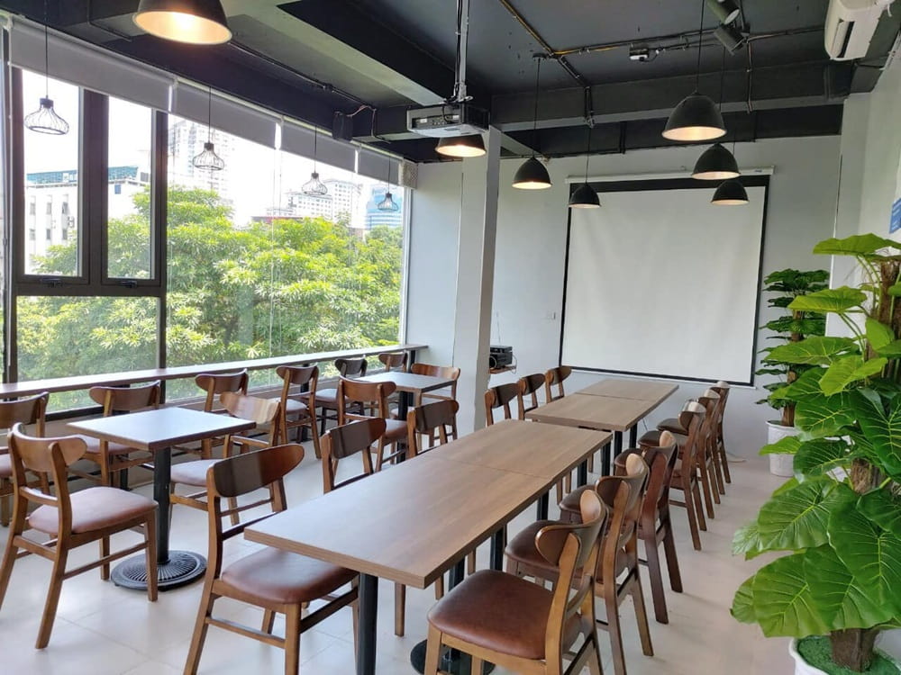 15 Quán Cafe Chùa Láng Với Không Gian Thư Giãn Tuyệt Đẹp 12 Phòng họp với bàn ghế gỗ, màn chiếu trắng, cây xanh và cửa sổ lớn nhìn ra cảnh quan bên ngoài.