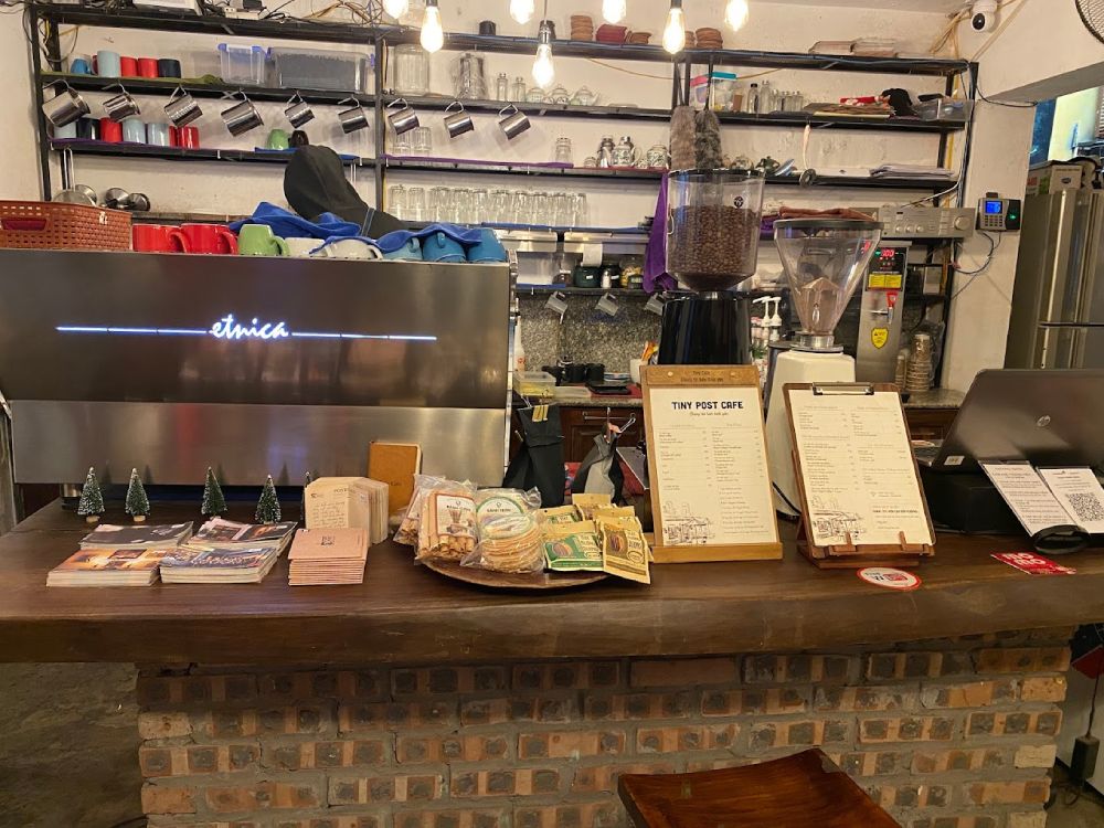 Khám Phá 11 Quán Cafe Đội Cấn Tuyệt Vời Cho Thư Giãn Và Làm Việc 5 Quầy bar quán cà phê với máy pha cà phê, thực đơn, đồ ăn nhẹ và kệ chứa cốc, ly phía sau.