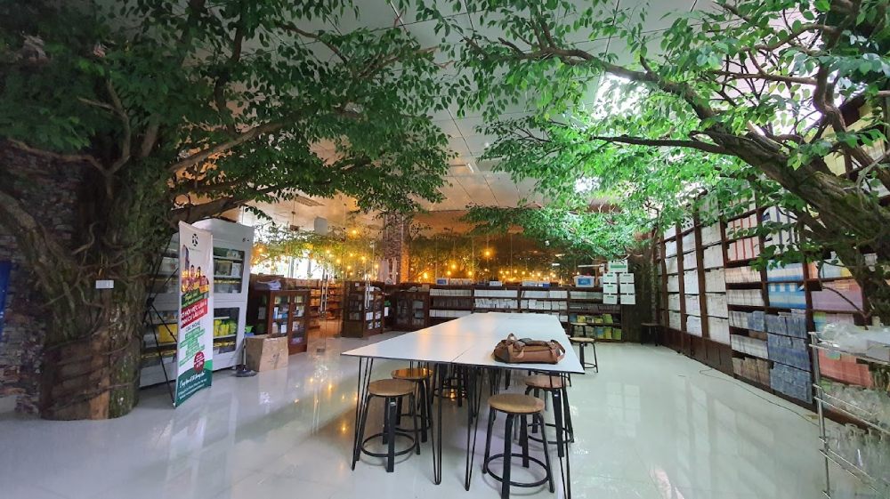 Khám Phá 11 Quán Cafe Sách Độc Đáo Tại Cầu Giấy Hút Hồn Độc Giả 7 Không gian thư viện với cây xanh và bàn ghế, xung quanh là kệ sách được chiếu sáng bằng đèn vàng.