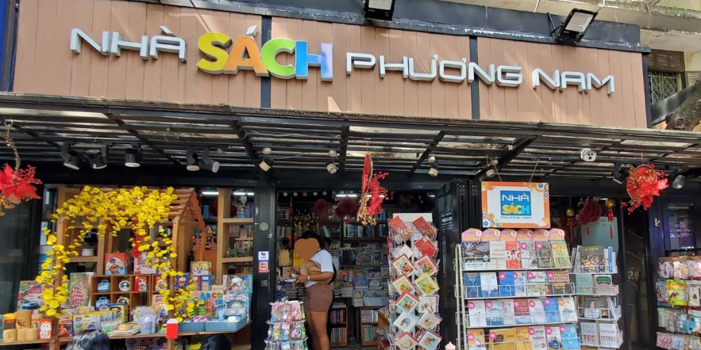 Khám Phá Top Quán Cafe Sách Hot Nhất Quận 1 Bạn Không Thể Bỏ Lỡ Năm Nay 3 Mặt tiền nhà sách với bảng hiệu và nhiều sách, tạp chí được trưng bày bên ngoài.