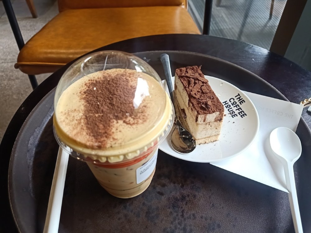 Khám Phá 11 Quán Cafe Đội Cấn Tuyệt Vời Cho Thư Giãn Và Làm Việc 14 Ly cà phê đá và miếng bánh tiramisu trên bàn, cạnh đó là thìa và ống hút nhựa.