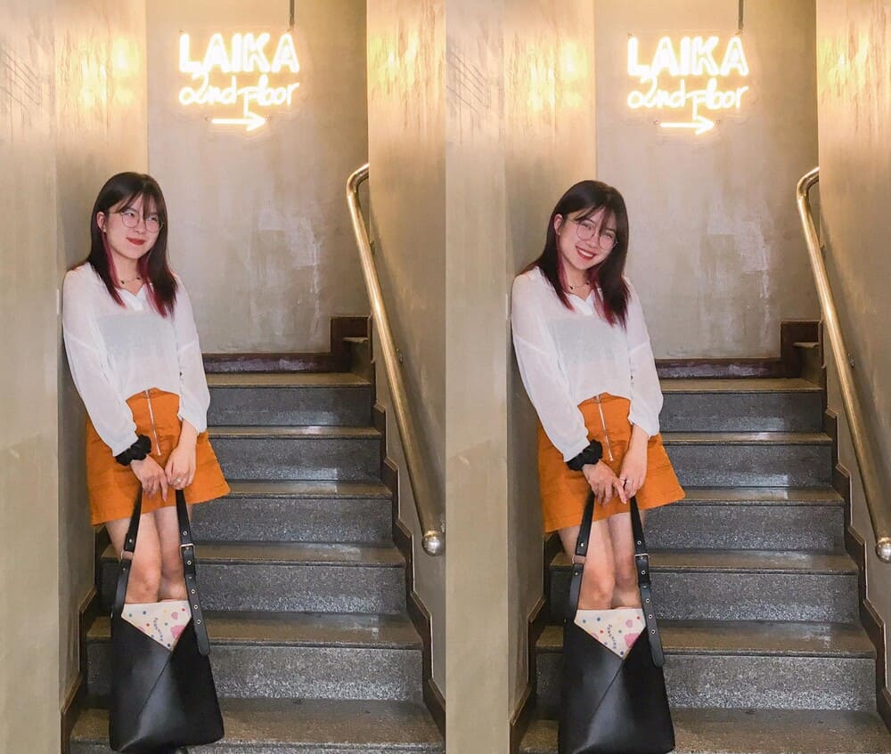 Khám Phá 15 Quán Cafe Hấp Dẫn Trên Đường Nguyễn Thị Định 18 Người đứng trên cầu thang, bên cạnh biển hiệu sáng đèn "LAIKA 2nd floor", cầm túi xách đen.