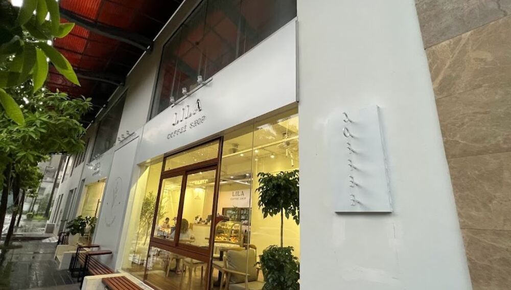 Khám Phá 9 Quán Cafe Độc Đáo Trên Đường Hoàng Hoa Thám 19 Mặt tiền quán cà phê hiện đại với cửa kính lớn, cây xanh bên ngoài và ánh sáng ấm áp từ bên trong.