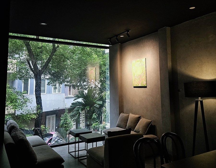 Khám Phá Top 10 Quán Cafe Giảng Võ Hấp Dẫn Nhất Tại Hà Nội 23 Phòng khách hiện đại với cửa kính lớn nhìn ra cây xanh bên ngoài, có ghế sofa, tranh treo và đèn đứng.