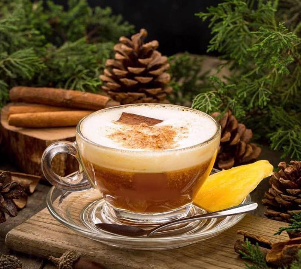 15 Quán Cafe Chùa Láng Với Không Gian Thư Giãn Tuyệt Đẹp 18 Tách cà phê với bọt sữa, rắc bột quế, trang trí lát gỗ quế và trái cây, nền có cành thông và quả thông.