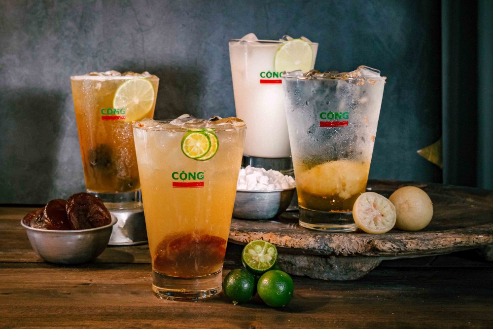 Khám Phá Top 10 Quán Cafe Giảng Võ Hấp Dẫn Nhất Tại Hà Nội 18 Bốn ly nước giải khát với đá, chanh và các nguyên liệu khác, được bày trên bàn gỗ, kèm theo chanh tươi và mơ khô.