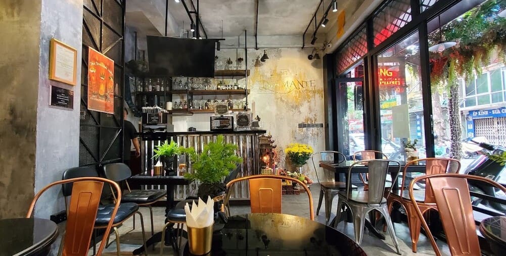 Khám Phá Top 10+ Quán Cafe Quán Thánh Lý Tưởng cho Hẹn Hò, Làm Việc và Thư Giãn 23 Quán cà phê trang trí hiện đại với bàn ghế kim loại và cây xanh, ánh sáng tự nhiên từ cửa kính lớn.