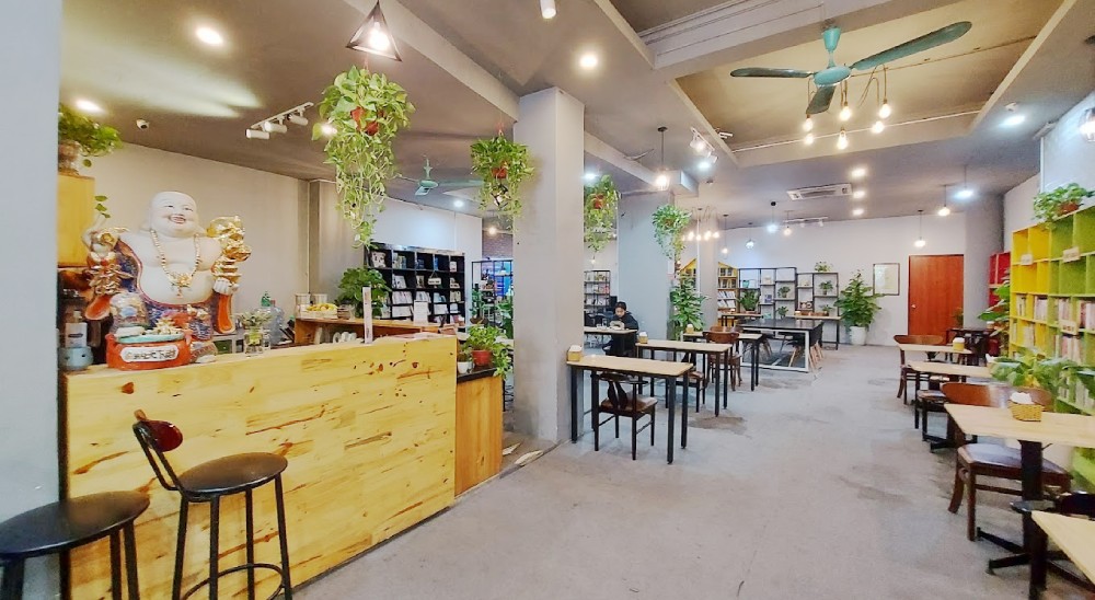 Khám Phá 12+ Quán Cafe Đẹp Ở Tây Sơn Với Đồ Uống Ngon 10 Quán cà phê với bàn ghế gỗ, cây xanh trang trí và kệ sách, tạo không gian ấm cúng và thư giãn.