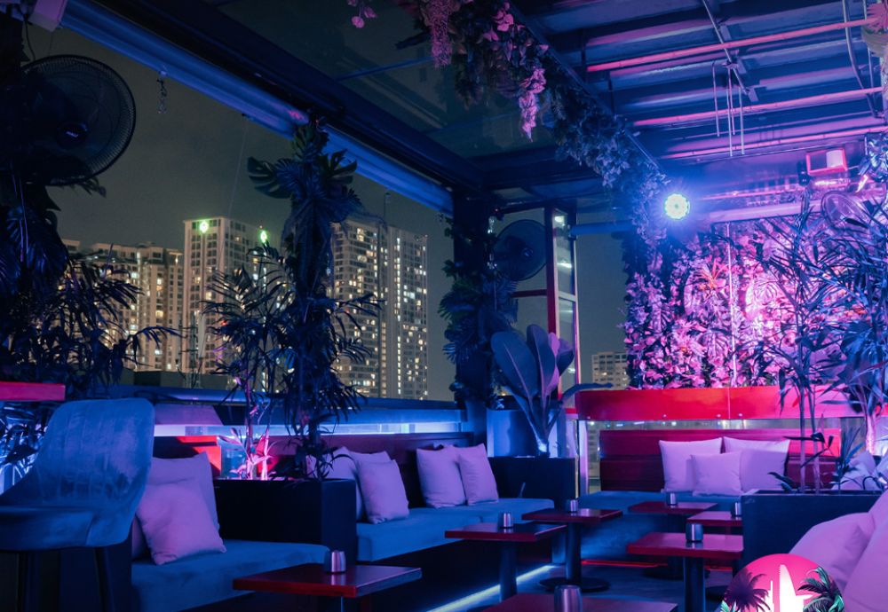 Khám Phá Top 10 Quán Rooftop Quận 1: View Đẹp Ngắm Thành Phố, Trải Nghiệm Thư Giãn Tuyệt Đỉnh 10 Quán bar rooftop với ánh sáng neon, cây xanh trang trí và tòa nhà cao tầng phía xa trong đêm.