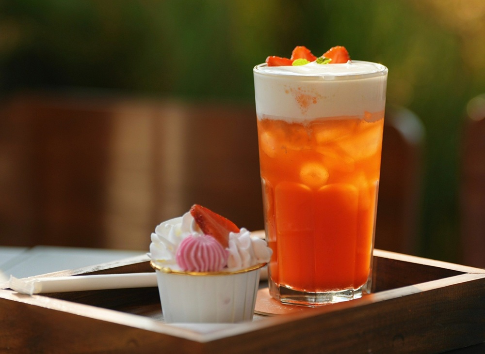 15 Quán Cafe Chùa Láng Với Không Gian Thư Giãn Tuyệt Đẹp 25 Ly trà sữa đá với lớp kem và dâu tây, bên cạnh là bánh nhỏ trang trí dâu tây trên khay gỗ.