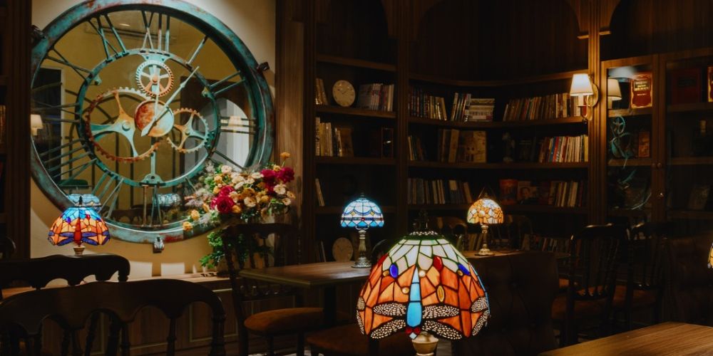 Khám Phá Top Quán Cafe Sách Hot Nhất Quận 1 Bạn Không Thể Bỏ Lỡ Năm Nay 15 Quán cà phê phong cách cổ điển với đồng hồ lớn, đèn trang trí nhiều màu sắc và giá sách đầy sách.