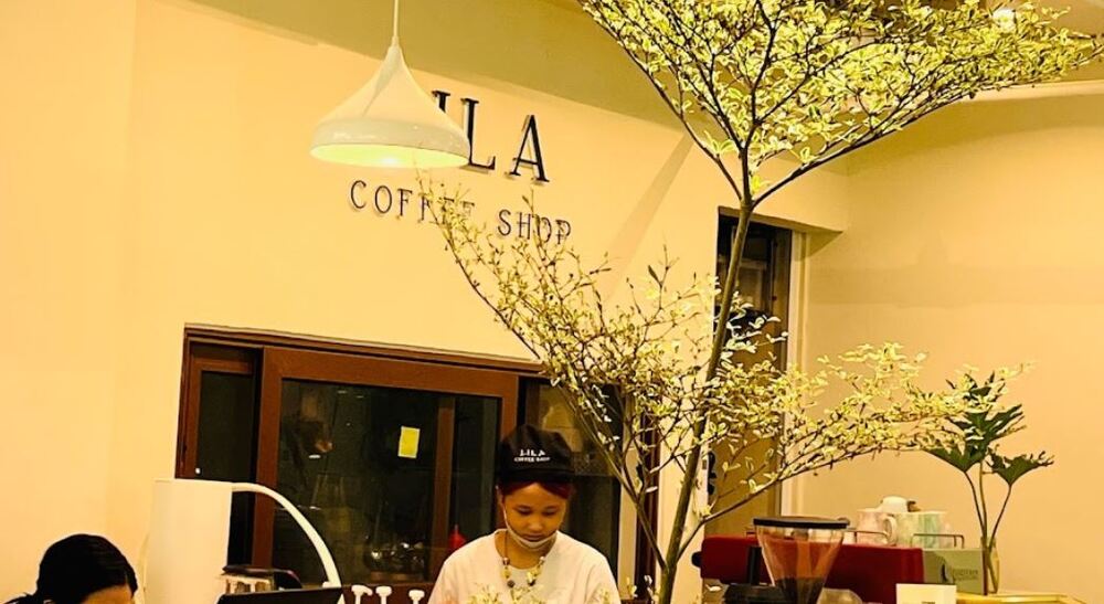 Khám Phá 9 Quán Cafe Độc Đáo Trên Đường Hoàng Hoa Thám 20 Quán cà phê với trang trí cây lớn bên trong, hai nhân viên chuẩn bị đồ uống sau quầy.