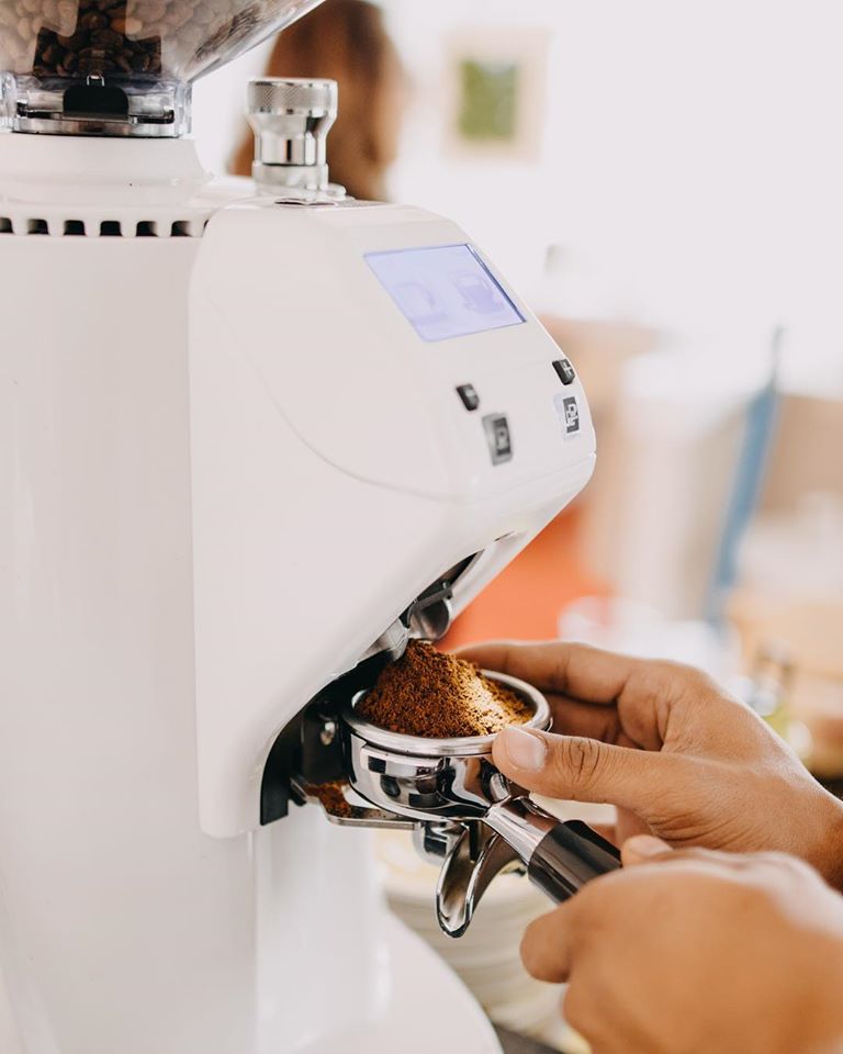 Người đang sử dụng máy xay cà phê để chuẩn bị bột cà phê vào tay cầm pha chế espresso.