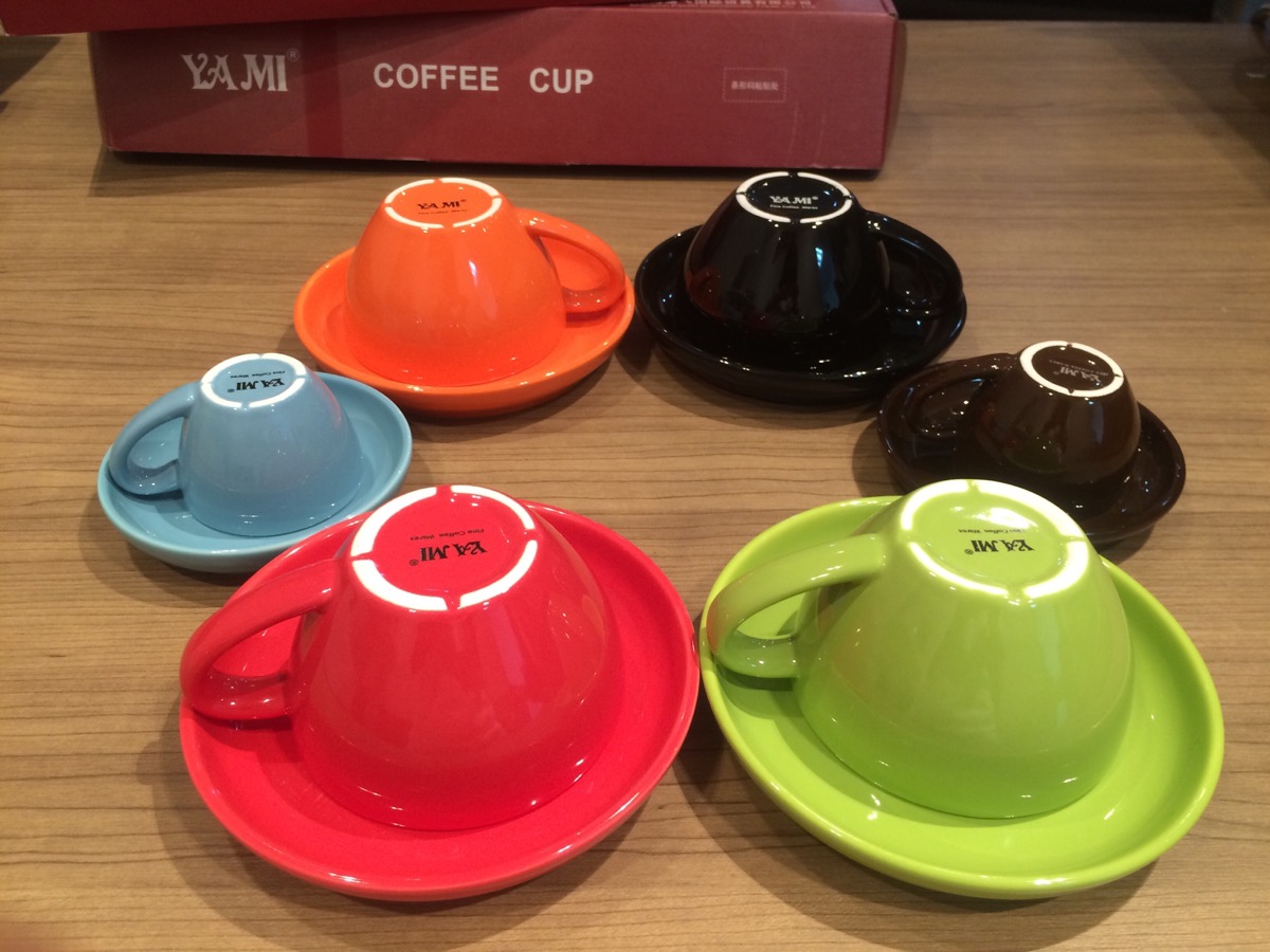 Nhiều tách và đĩa lót màu sắc khác nhau được úp ngược trên bàn gỗ, cạnh hộp đựng màu đỏ.