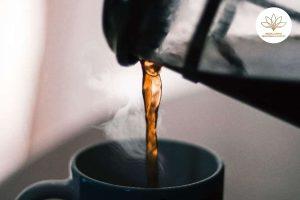 Nước cà phê đang được rót từ bình vào một chiếc cốc, với hơi nước nhẹ bốc lên.