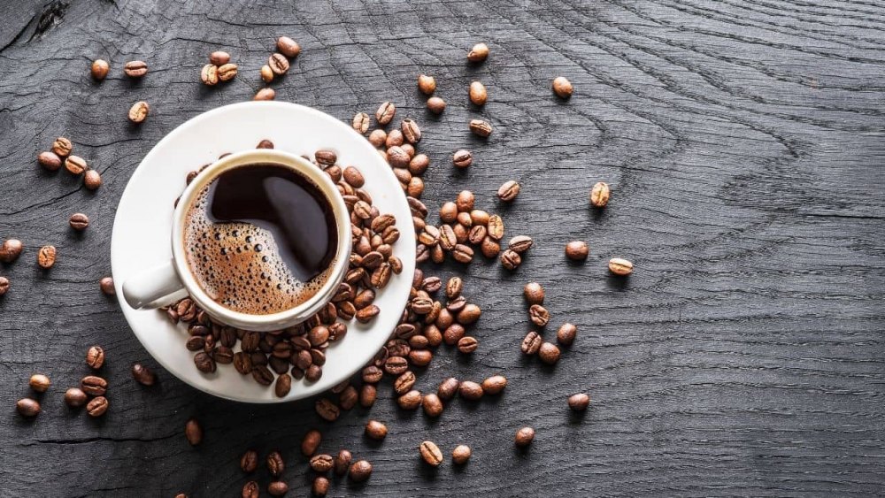 loi-ich-cua-ca-phe-decaf Tách cà phê trên bàn gỗ đen, xung quanh có nhiều hạt cà phê rải rác.