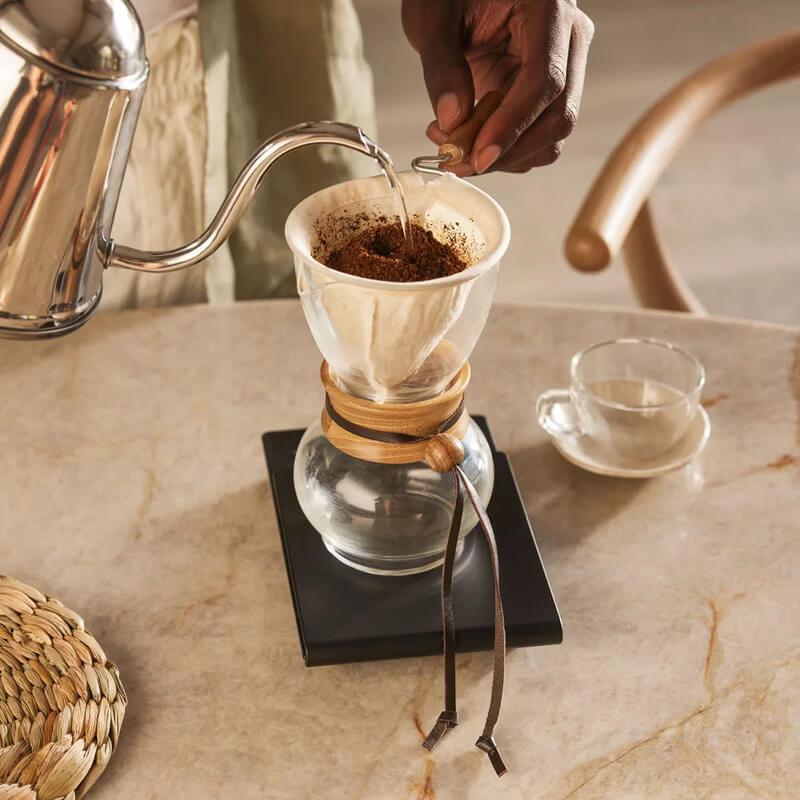 Người đang pha c&agrave; ph&ecirc; bằng phương ph&aacute;p pour-over với b&igrave;nh lọc v&agrave; ấm nước tr&ecirc;n b&agrave;n đ&aacute; cẩm thạch.