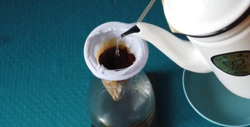 nel-drip-coffee-8 Ấm nước đang rót nước nóng vào phin lọc cà phê bằng vải trên bình thủy tinh.