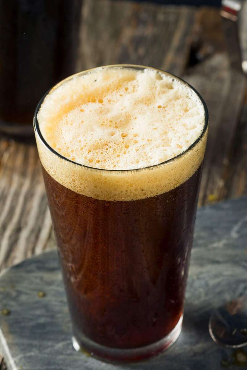 Ly bia n&acirc;u với bọt trắng tr&ecirc;n bề mặt, đặt tr&ecirc;n b&agrave;n gỗ tối m&agrave;u.