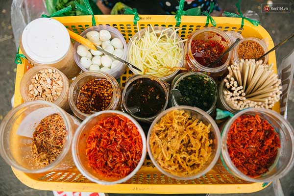 Các hũ đựng nguyên liệu và gia vị đa dạng trên một khay nhựa, gồm tôm khô, trứng cút, xoài bào, và các loại sốt.