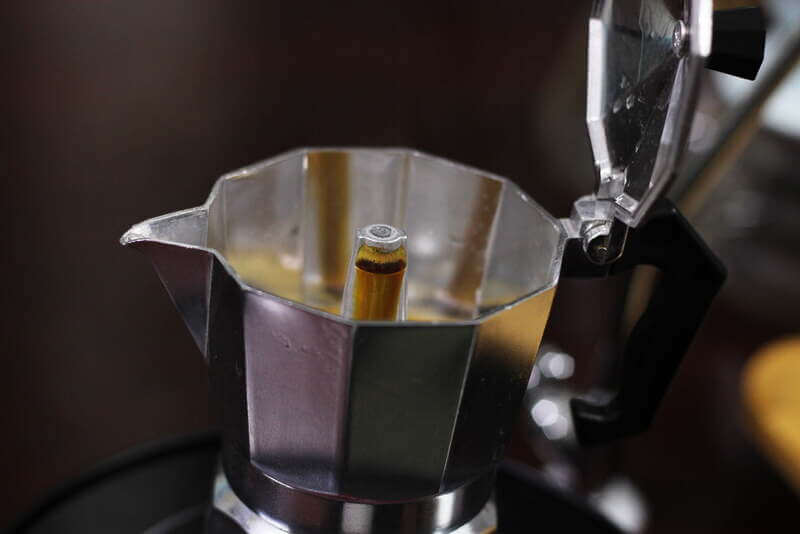 Ấm pha c&agrave; ph&ecirc; moka bằng kim loại đang mở nắp, với c&agrave; ph&ecirc; đang chảy qua ống trung t&acirc;m.