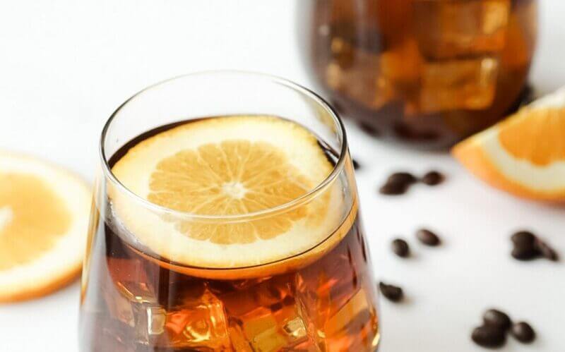 Ly đồ uống c&oacute; l&aacute;t cam, đ&aacute; vi&ecirc;n, hạt c&agrave; ph&ecirc; xung quanh, nền trắng.