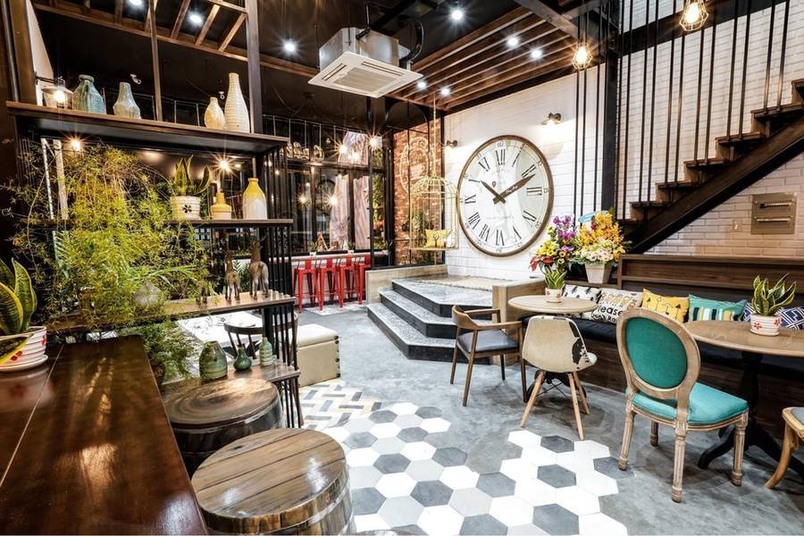 Kh&ocirc;ng gian nội thất qu&aacute;n c&agrave; ph&ecirc;, trang tr&iacute; với đồng hồ lớn, b&agrave;n ghế, c&acirc;y xanh v&agrave; &aacute;nh s&aacute;ng ấm &aacute;p.