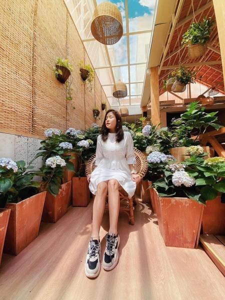 Người ngồi tr&ecirc;n ghế giữa vườn hoa cẩm t&uacute; cầu, &aacute;nh s&aacute;ng tự nhi&ecirc;n chiếu qua m&aacute;i k&iacute;nh, kh&ocirc;ng gian tho&aacute;ng đ&atilde;ng.